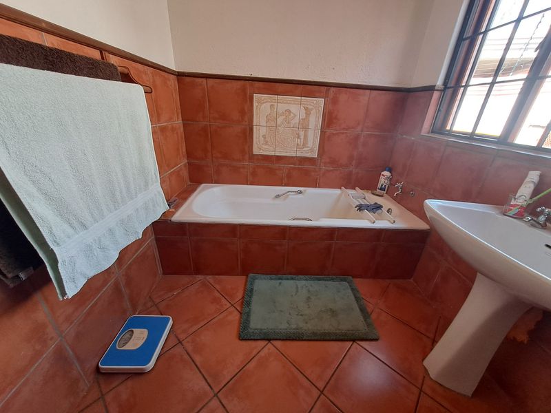A dated bathroom featuring terracotta-style ceramic tiling, a built-in bathtub, and a white pedestal washbasin.