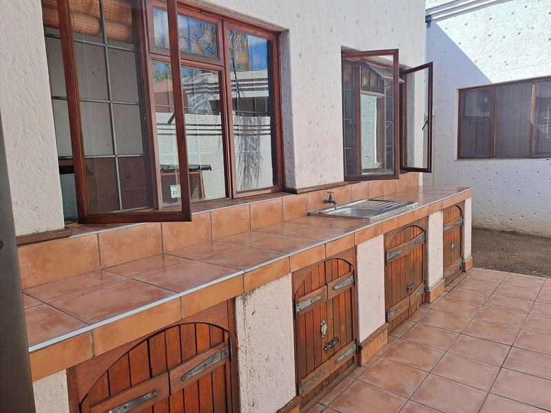Outdoor patio area featuring a built-in tiled prep station with sink, wooden cabinetry, and large timber-framed windows overlooking the exterior space.
