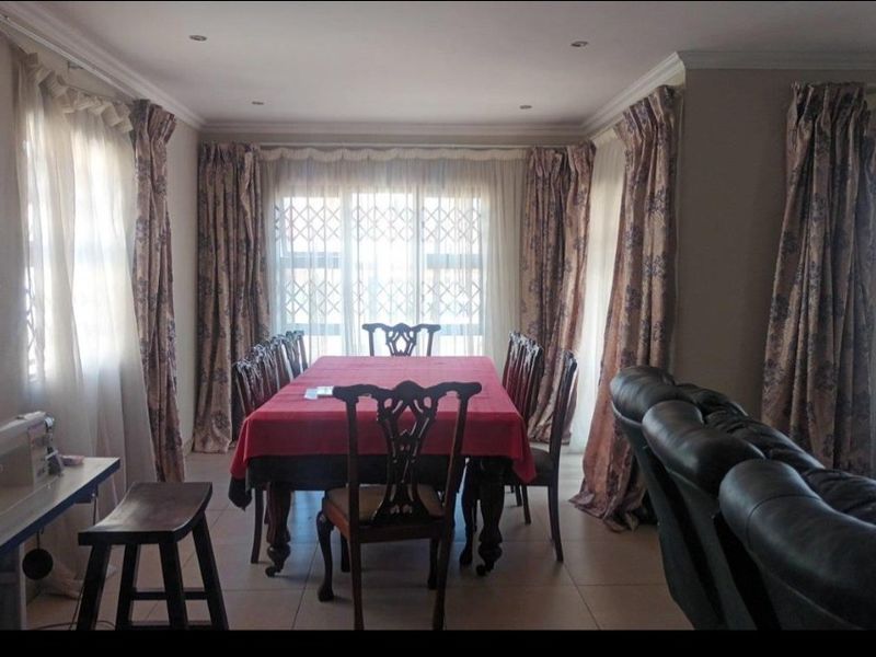 A dining room featuring tiled flooring, recessed ceiling details, and large windows fitted with security gates and curtains.