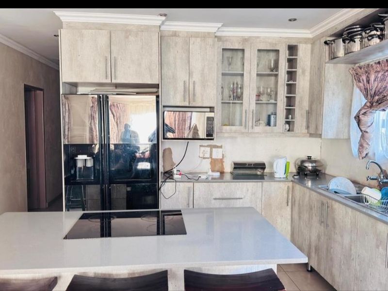 Kitchen featuring light wood-grain cabinetry, a central island with an integrated electric hob, and a stainless steel sink.