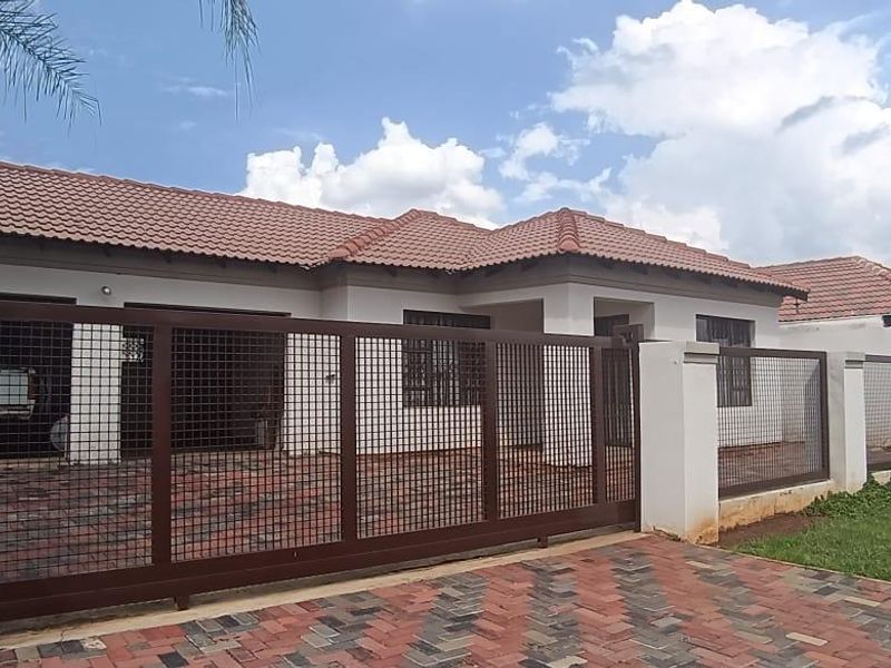Front view of a single-story house featuring a tiled roof, paved driveway, and a secure sliding metal gate with a boundary wall.