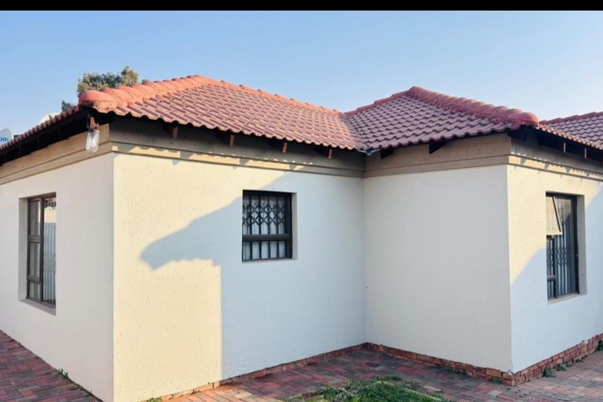 Rear exterior view of the house featuring terracotta roof tiles, plastered walls, and paved patio area with security bars on windows.