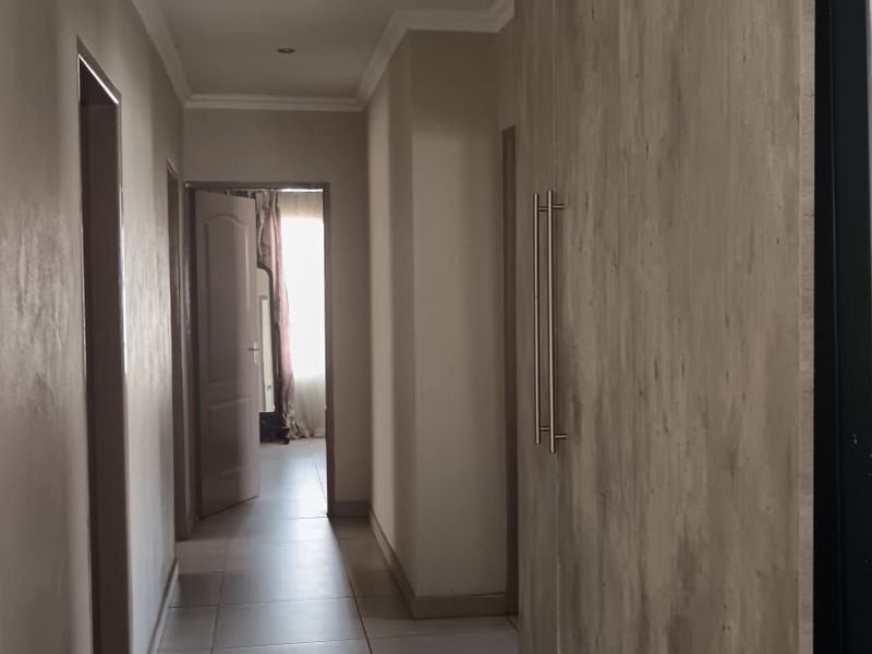 A clean, neutral hallway featuring tiled flooring, recessed lighting, and built-in cabinetry, providing a seamless transition between living spaces.