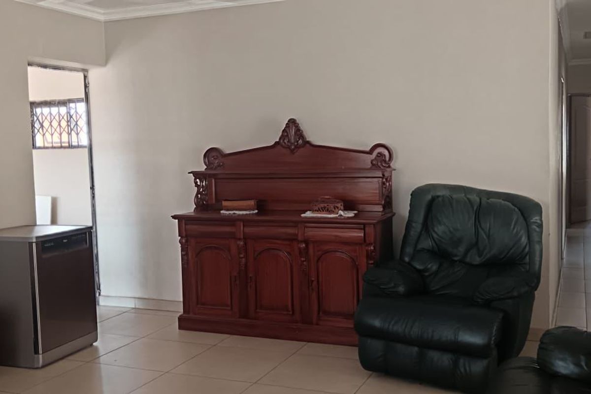A spacious living area featuring neutral wall tones, tiled flooring, and decorative ceiling cornicing, providing a functional and well-lit space.