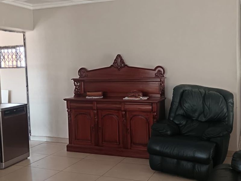 A spacious living area featuring neutral wall tones, tiled flooring, and decorative ceiling cornicing, providing a functional and well-lit space.