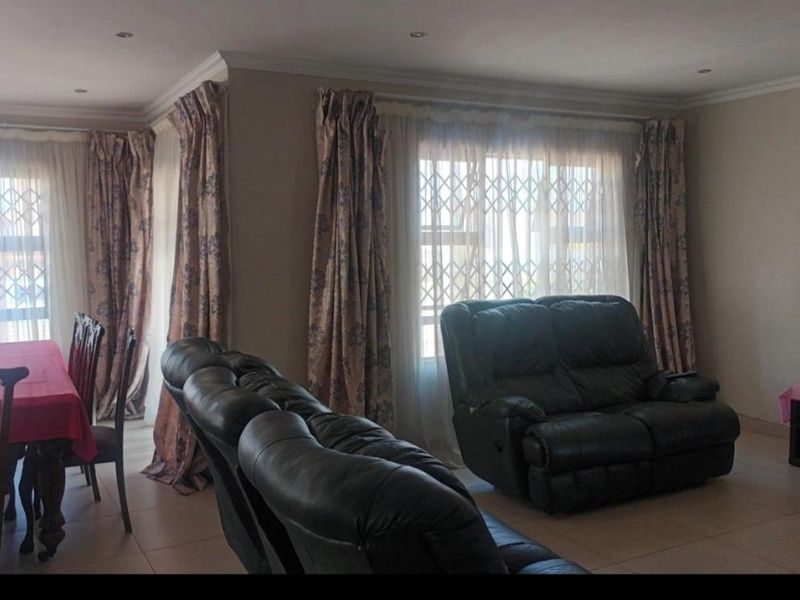 Spacious open-plan living and dining area featuring tiled flooring, recessed lighting, and large windows with security gates.