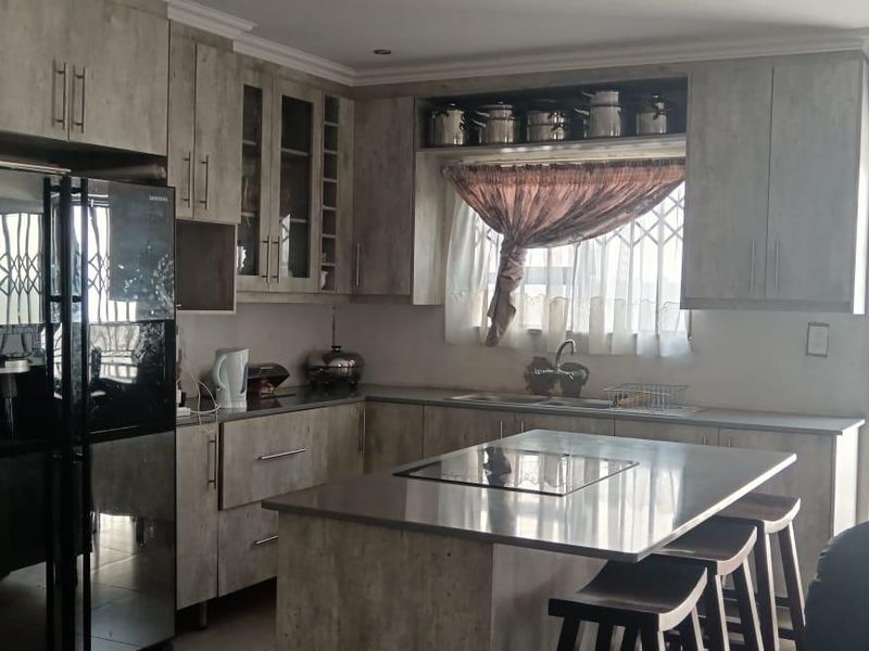 Modern kitchen featuring wood-look cabinetry, a central island with a cooktop, and a secure exterior door with a metal security gate.