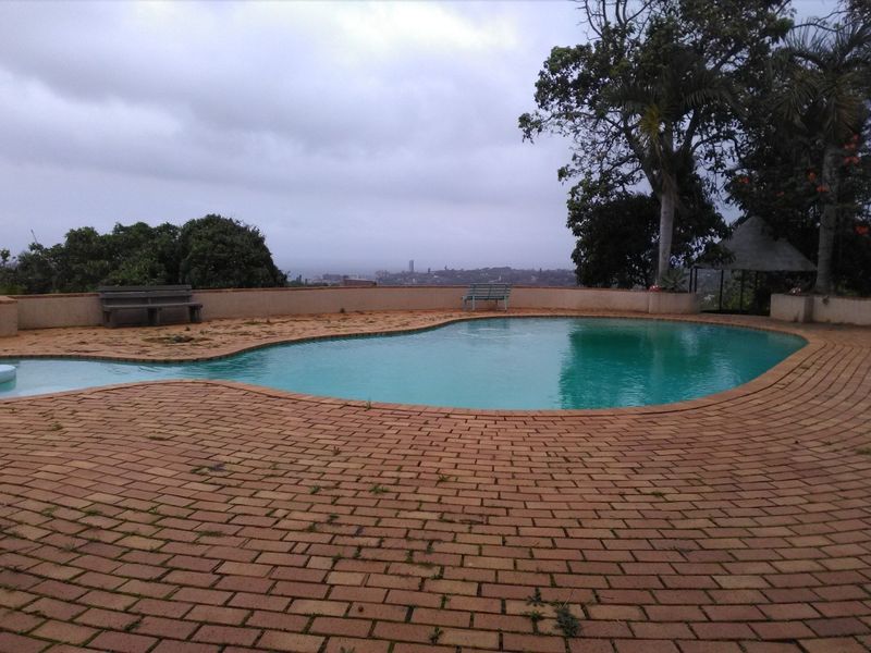 Outdoor swimming pool area featuring brick paving and a retaining wall with distant views.