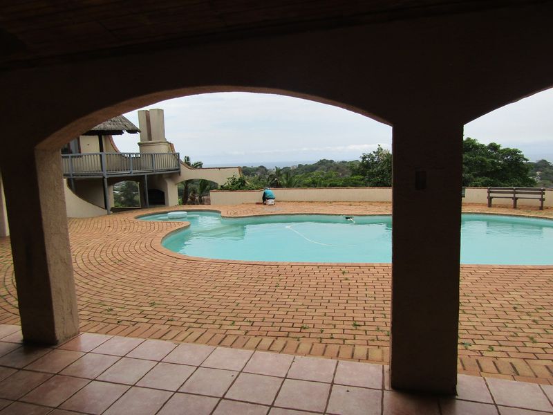 Outdoor pool area featuring a brick-paved deck, arched covered patio, and elevated balcony with scenic views.