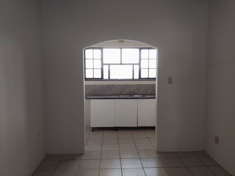 A functional kitchen space featuring white cabinetry, a stainless steel sink, tiled splashback, and tiled flooring, viewed through an arched doorway.