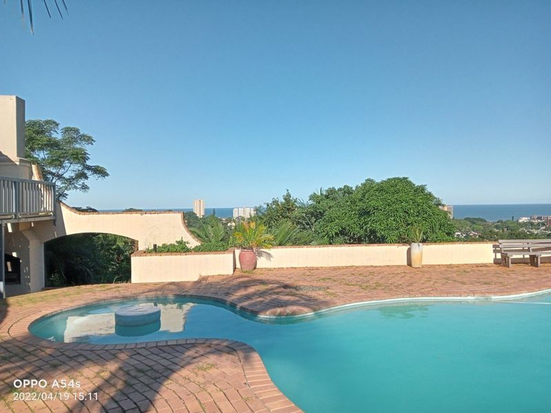 Outdoor pool area featuring a brick-paved deck, masonry boundary wall, and elevated patio structure with scenic coastal views.