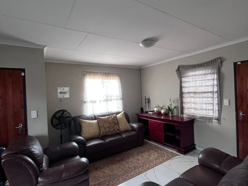 A living room featuring white marble-look floor tiles, neutral wall paint, and timber doors, providing a functional and well-maintained living space.