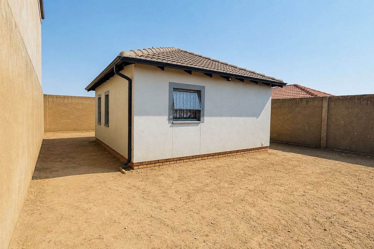 Rear view of the property featuring a tiled roof, plastered exterior walls, and a large, undeveloped yard enclosed by high perimeter walls.