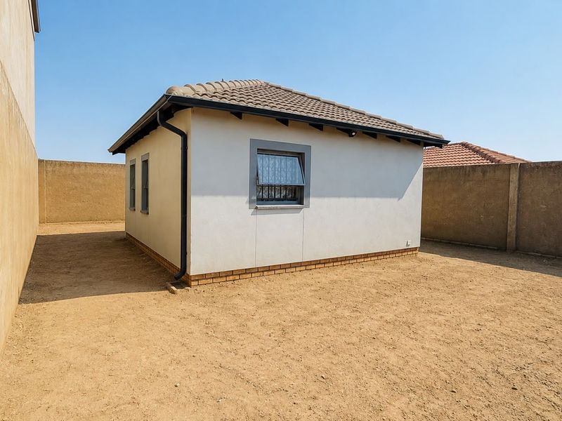 Rear view of the property featuring a tiled roof, plastered exterior walls, and a large, undeveloped yard enclosed by high perimeter walls.
