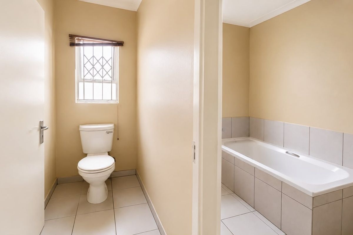 A functional bathroom featuring a separate toilet area and a tiled bathtub, finished with neutral wall tones and ceramic floor tiles.