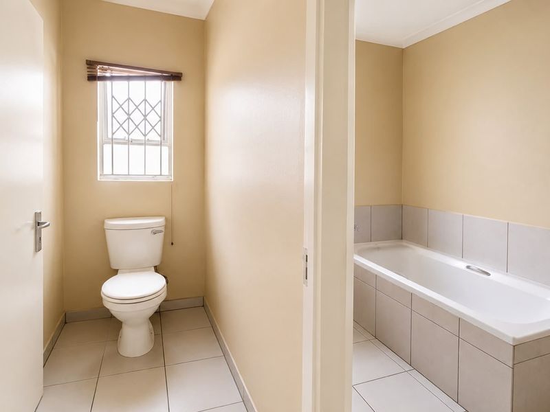 A functional bathroom featuring a separate toilet area and a tiled bathtub, finished with neutral wall tones and ceramic floor tiles.