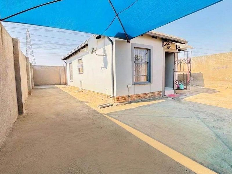 Rear exterior view of the property featuring a paved yard, perimeter walling, and a blue shade sail structure over the outdoor area.
