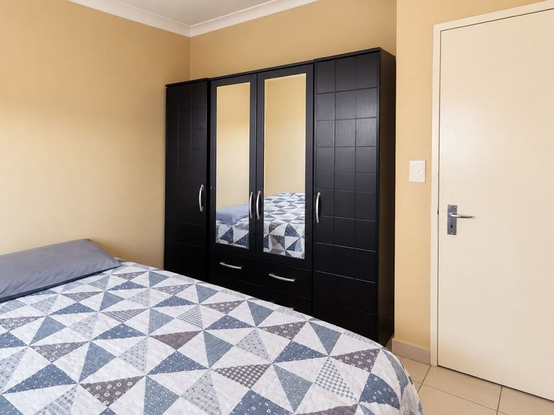 A functional bedroom featuring tiled flooring, neutral wall tones, and a built-in wardrobe with mirrored central panels.