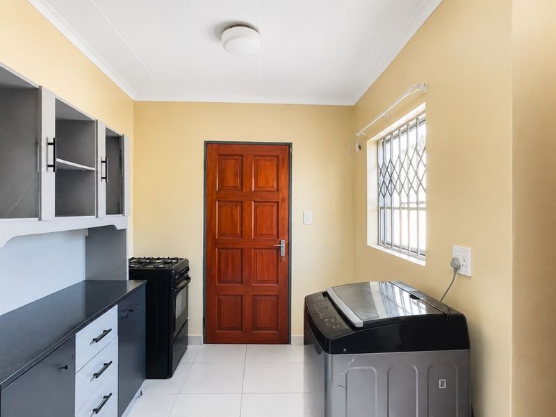 A functional scullery area featuring modern dark cabinetry, stone countertops, a gas stove, and tiled flooring with direct access to an exterior door.