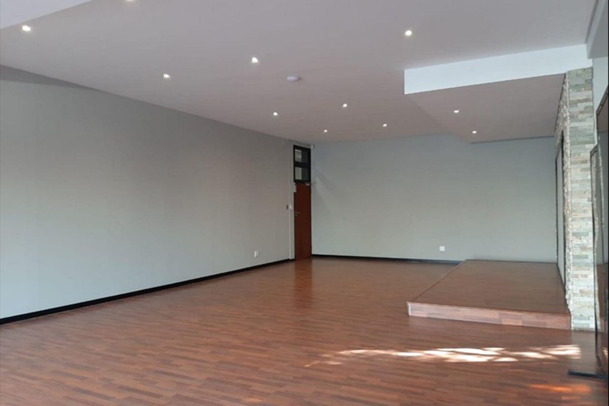A spacious, empty open-plan commercial area featuring laminate flooring, recessed downlighting, and a decorative stone-clad feature wall with a raised platform.