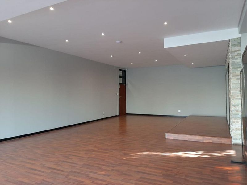A spacious, empty open-plan commercial area featuring laminate flooring, recessed downlighting, and a decorative stone-clad feature wall with a raised platform.