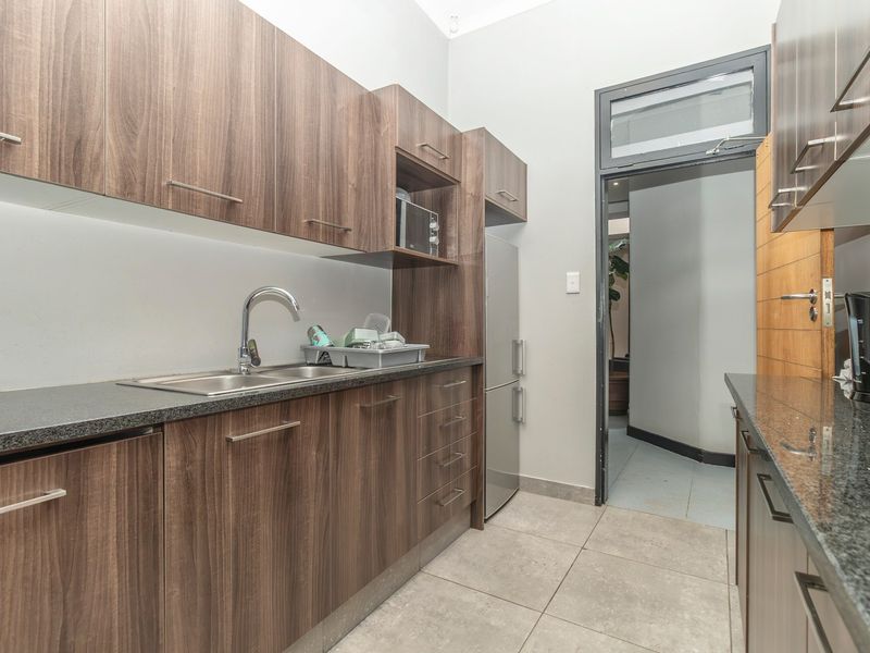 A functional scullery featuring modern wood-look cabinetry, granite countertops, a stainless steel double sink, and tiled flooring, providing efficient prep and wash-up space.