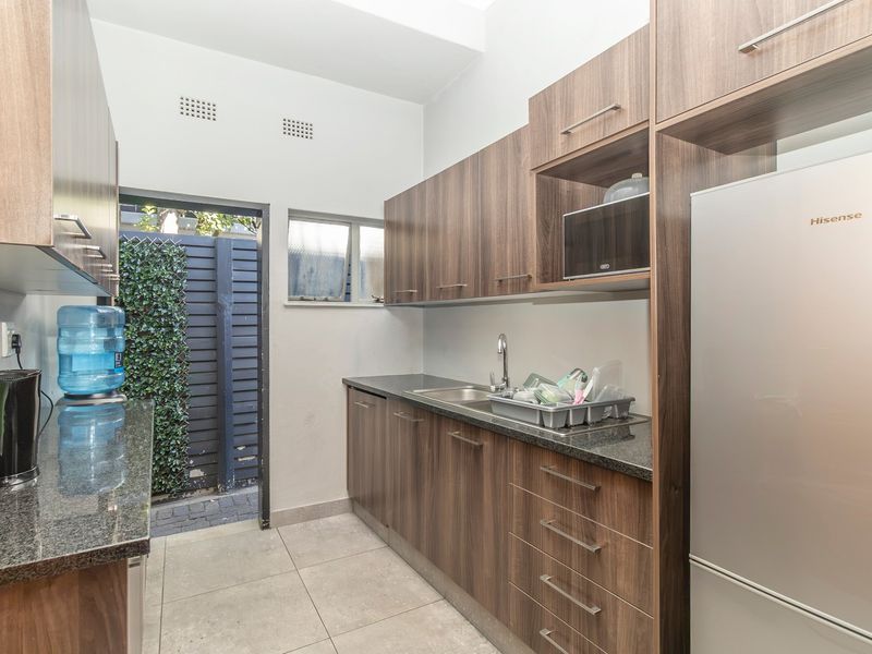 A functional scullery featuring modern wood-finish cabinetry, granite countertops, a stainless steel sink, and direct access to an outdoor area.