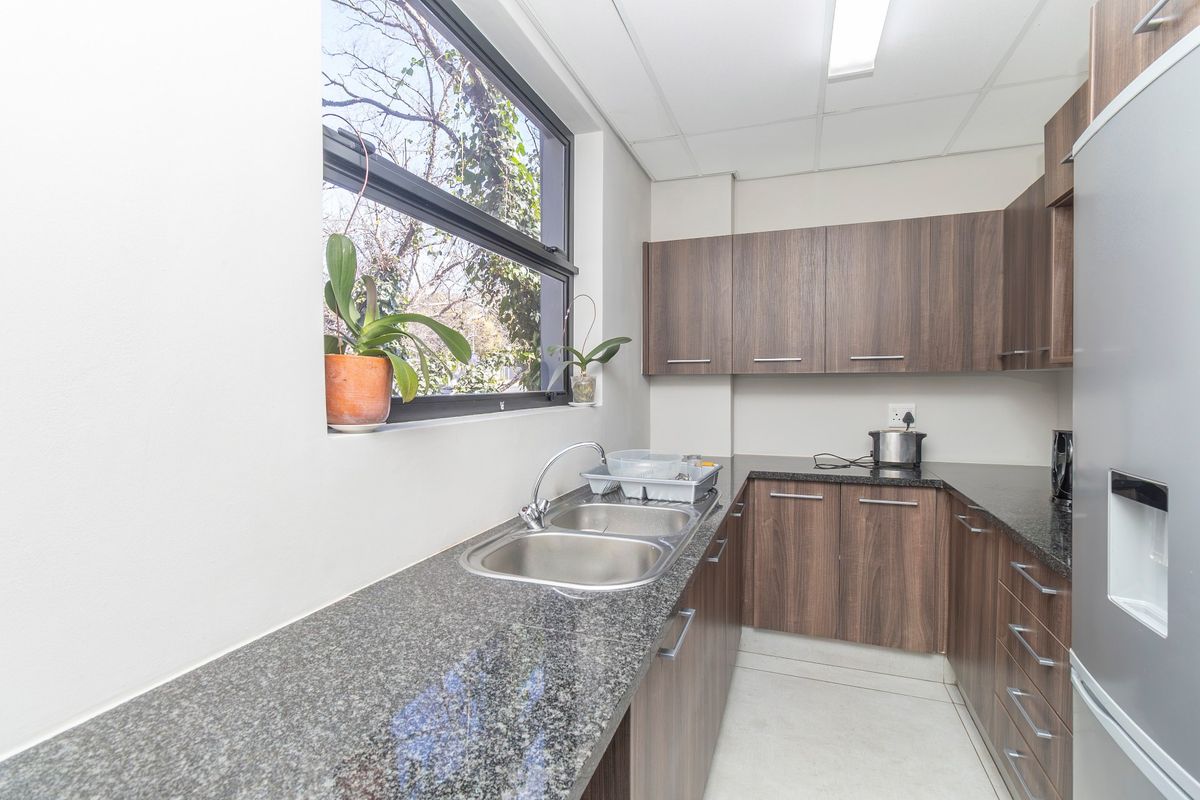 A functional kitchen area featuring dark wood-look cabinetry, granite countertops, a double stainless steel sink, and a drop ceiling with integrated lighting.