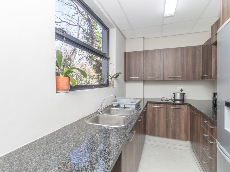 A functional kitchen area featuring dark wood-look cabinetry, granite countertops, a double stainless steel sink, and a drop ceiling with integrated lighting.
