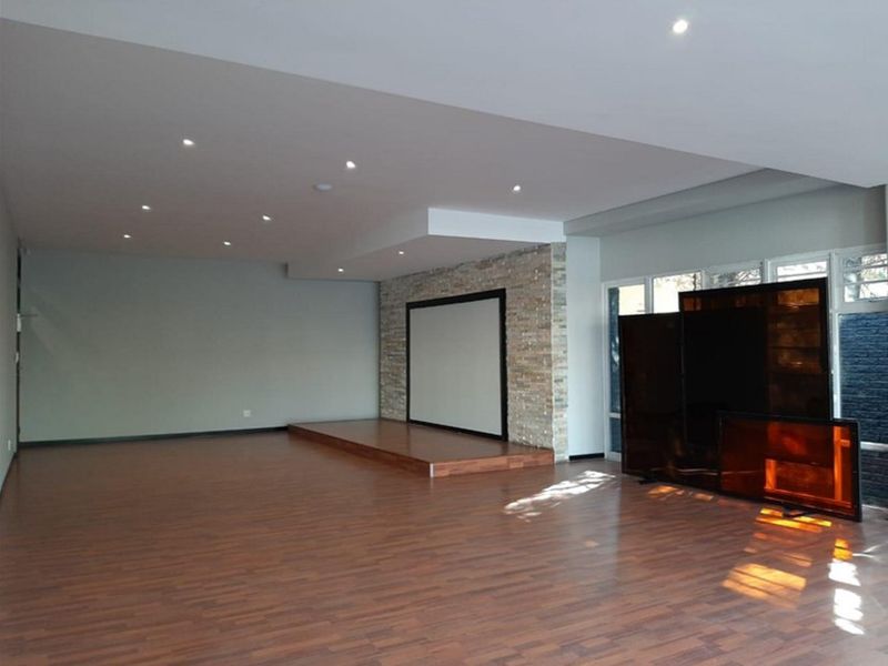 A spacious cinema room featuring a raised timber platform, a stone feature wall with a built-in projection screen, and recessed downlighting.