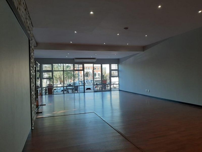 Spacious open-plan commercial area featuring laminate flooring, recessed lighting, a stone feature wall, and large glass windows providing ample natural light.