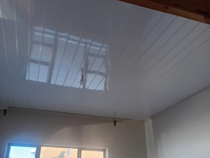 An empty bedroom featuring a glossy PVC panel ceiling with an exposed timber beam and aluminium window frames, currently requiring minor finishing work.