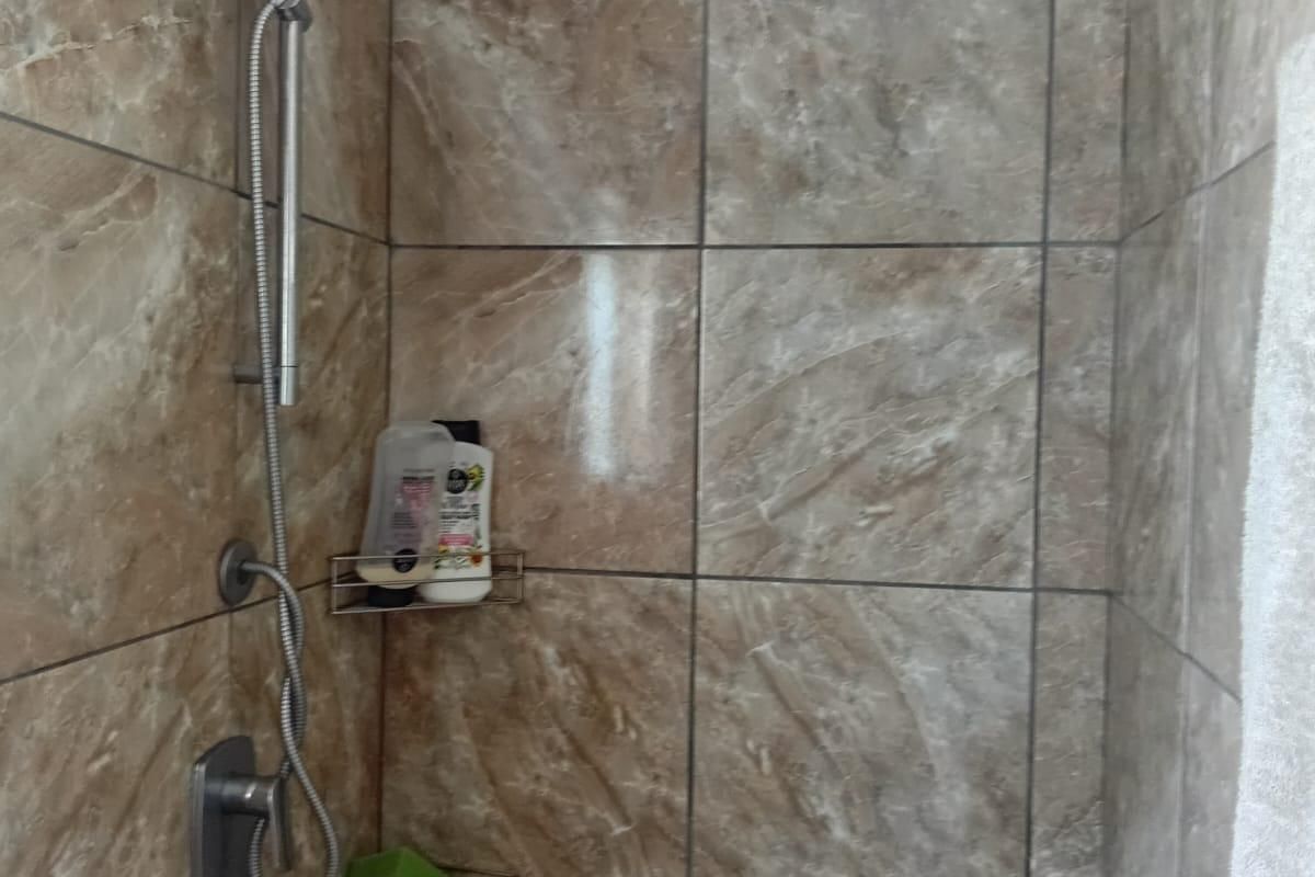 A shower enclosure featuring brown marble-effect wall tiles and a modern chrome shower fixture.