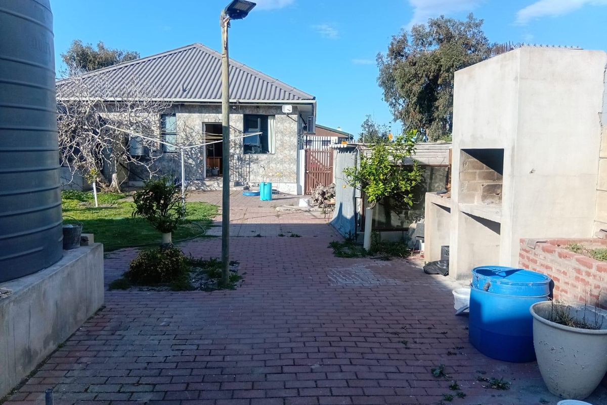 Rear exterior view featuring a brick paved patio, built-in braai area, and a large water storage tank set against the house structure.