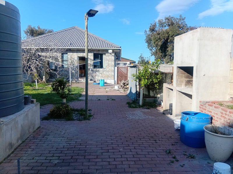 Rear exterior view featuring a brick paved patio, built-in braai area, and a large water storage tank set against the house structure.