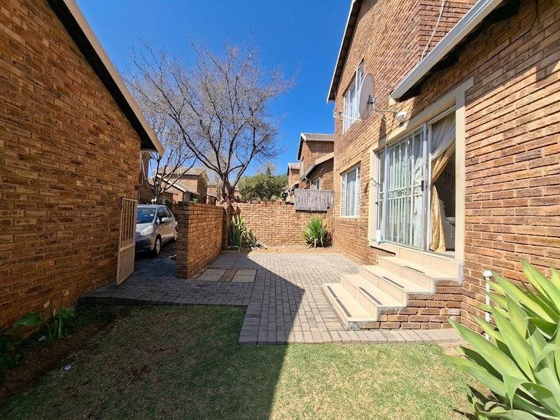 Rear exterior view of the townhouse featuring a paved patio area, brick facade, and sliding door access to the interior living space.