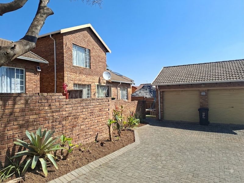Front view of a face brick townhouse featuring a double garage, paved driveway, and a low-maintenance garden with a brick boundary wall.