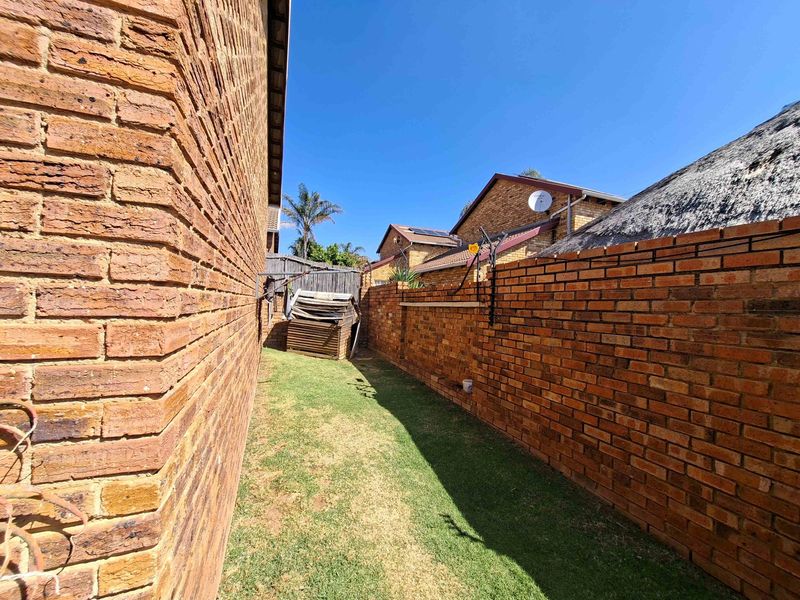 A narrow side garden area featuring brick boundary walls and a grass lawn, typical of a townhouse exterior side passage.