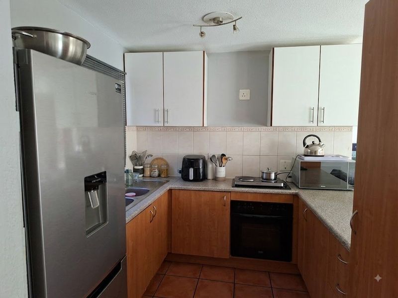 A functional U-shaped kitchen featuring wood-finish lower cabinetry, white upper cabinets, tiled backsplash, and built-in oven with hob.