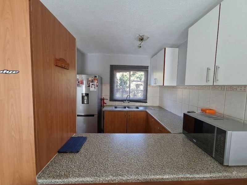 A functional kitchen featuring laminate countertops, a double bowl sink, tiled backsplash, and a mix of wood-tone and white cabinetry.