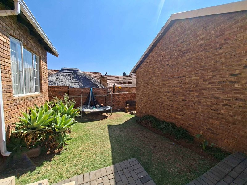 A private rear garden area featuring face brick exterior walls, a small lawn, and a paved walkway between townhouse structures.