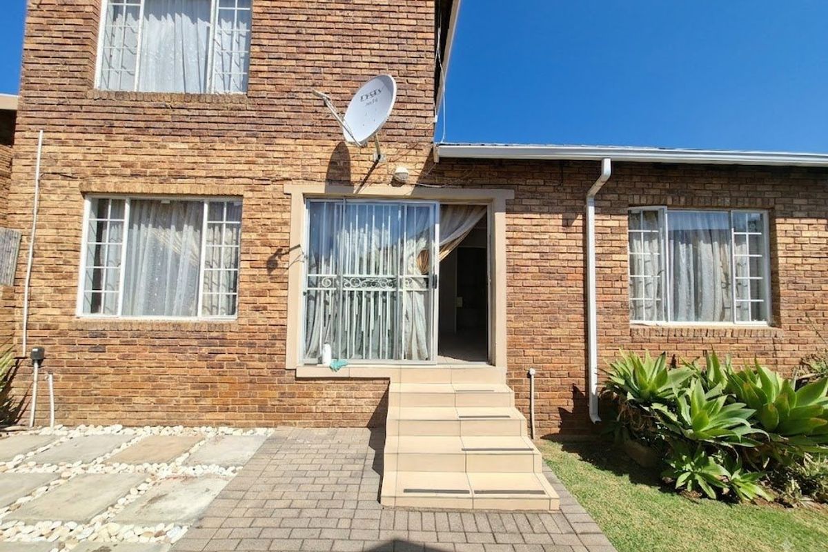 Rear exterior view of the townhouse featuring a brick facade, paved patio area, and tiled steps leading to a sliding glass door entrance.
