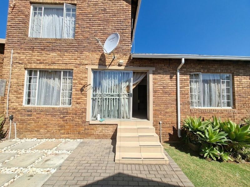 Rear exterior view of the townhouse featuring a brick facade, paved patio area, and tiled steps leading to a sliding glass door entrance.