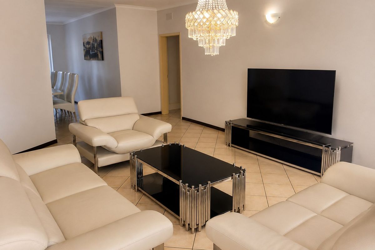 A well-maintained living room featuring ceramic floor tiles, a decorative crystal chandelier, and coved ceiling details, providing a bright and comfortable living space.