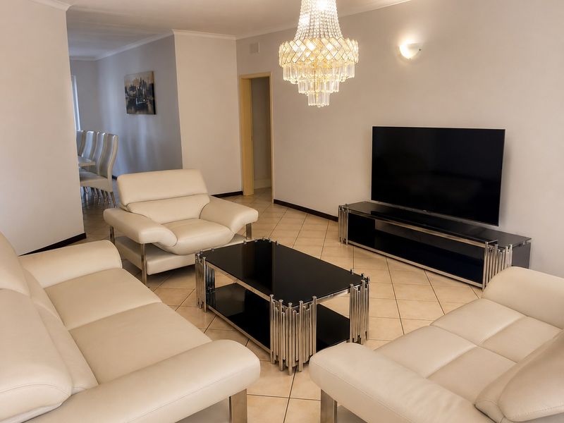 A well-maintained living room featuring ceramic floor tiles, a decorative crystal chandelier, and coved ceiling details, providing a bright and comfortable living space.