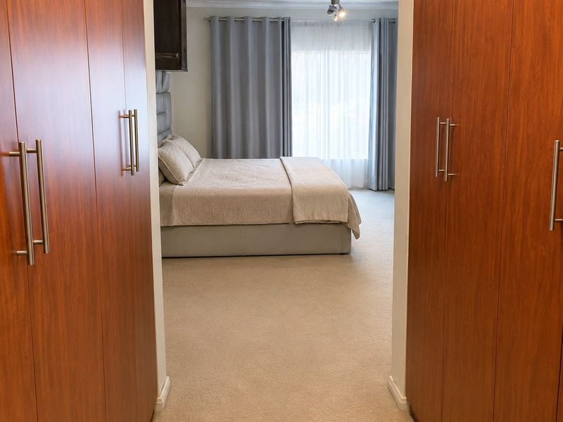 A well-maintained bedroom featuring neutral carpeting, a ceiling fan, and extensive built-in wooden cupboards providing ample storage space.