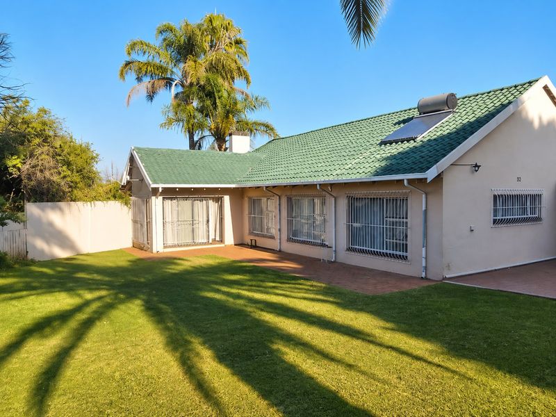 Rear view of the house featuring a green tiled roof, solar water heater, paved patio area, and a well-maintained lawn.