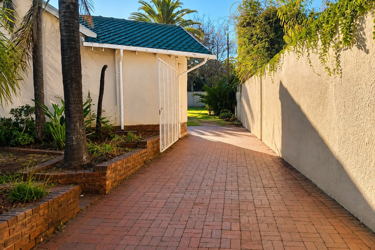 A well-maintained rear exterior area featuring a brick-paved pathway, brick retaining walls, and a secure gated entrance leading to the garden.