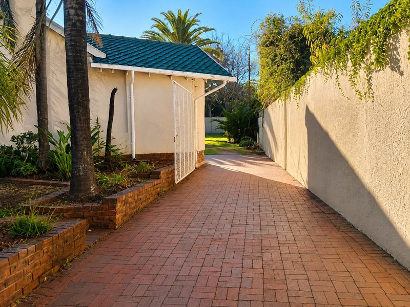 A well-maintained rear exterior area featuring a brick-paved pathway, brick retaining walls, and a secure gated entrance leading to the garden.