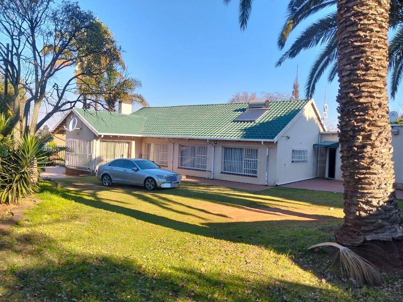 Rear view of a single-story house featuring a green tiled roof, solar water heater, security bars on windows, and a spacious garden.